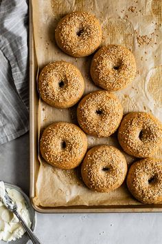 six bagels with sesame sprinkles on a baking sheet next to butter