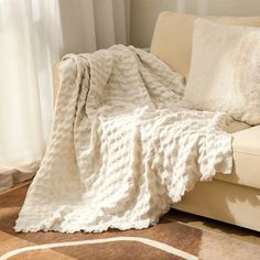 a couch with a white blanket on top of it next to a rug and window