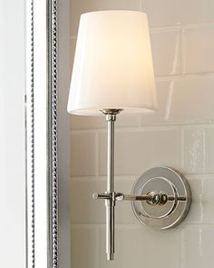 a bathroom light with a white shade on the wall next to a mirror and sink