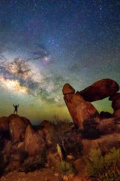 a man standing on top of a rock formation under the night sky