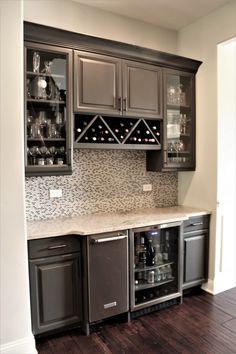 a kitchen with gray cabinets and wine racks on the back wall, along with dark wood flooring