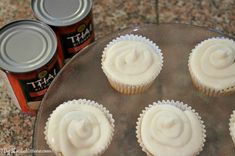 six cupcakes with frosting sitting on top of a cake pan next to cans of beer