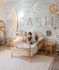 a young child sitting on top of a bed next to a wallpapered room