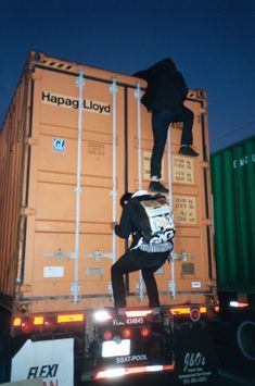 a man standing on the back of a truck with shipping containers in the back ground