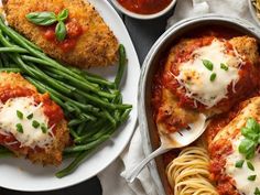 two white plates topped with meatballs and pasta next to green beans, sauce and parmesan cheese