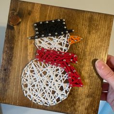 a string art snowman made with red, white and black strings on a wooden board