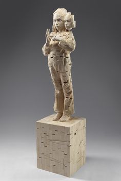 a sculpture of a woman standing on top of a block of wood with her arms crossed