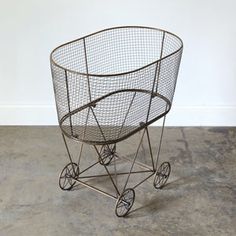 a metal wire basket with wheels on concrete floor next to white wall and gray cement floor