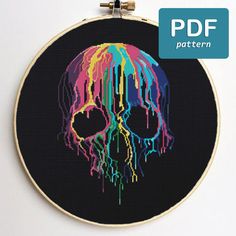 a cross stitch pattern with a colorful skull in the center on a black background that is framed by a circular hoop