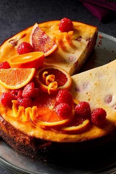 a cake with oranges and raspberries on it sitting on top of a plate