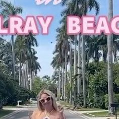 a woman standing on the side of a road with palm trees in front of her