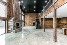 an empty living room with stone fireplace and wood paneled walls, large windows on the second floor