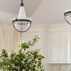 a vase filled with white flowers sitting on top of a kitchen counter next to two hanging lights