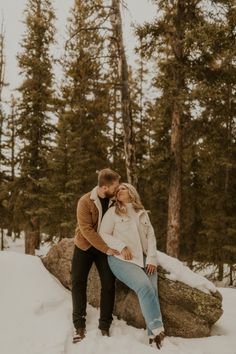 a man and woman standing next to each other on top of snow covered ground in front of trees