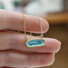 For writing inspiration. This necklace reverses for two creativity-themed messages. "write" is written on aquamarine enamel, and "create" is written on white enamel.Made from gold dipped sterling silver, small and wearable at only 3/4" wide by just over 1/4" tall. Enameled in my Oakland, California workshop, it comes with a 16, 18 or 20 inch gold filled chain. Choose your length from the drop down menu. Each piece is cast in sterling silver, to which 3 layers of vitreous enamel are applied and f Inspirational Blue Jewelry As A Gift, Inspirational Blue Jewelry For Gifts, Blue Personalized Inspirational Jewelry, Engraved Enamel Necklace For Gifts, Elegant Personalized Enamel Jewelry, Blue Engraved Enamel Necklaces, Personalized Silver Charm Necklace With Enamel, Personalized Gold Enamel Charm Necklace, Enamel Necklaces