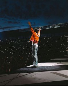 a man standing on top of a stage holding his arms up in the air while wearing an orange shirt