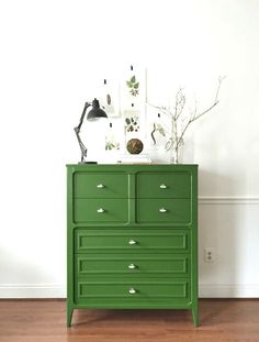 a green chest of drawers sitting on top of a hard wood floor next to a white wall