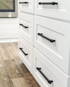 white cabinets with black handles and knobs in a kitchen, next to a microwave