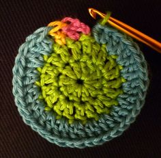 a crocheted pot holder with a yellow and pink flower on it next to a knitting needle