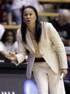 a female basketball player in a white suit and black shirt is on the court with her hand out