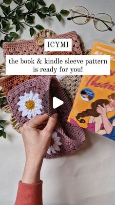 a person holding up a crocheted purse next to a book and some books