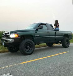 a woman is sitting in the bed of a green truck with her dog on the back