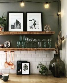 two framed pictures are hanging on the wall above a shelf with wine glasses and utensils