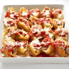 a white casserole dish filled with shells covered in marinara sauce and cheese