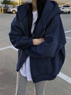 a woman wearing a face mask standing in a parking lot with her arms crossed and looking at the camera