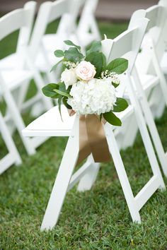 white folding chairs with flowers and greenery tied to the back are sitting on grass