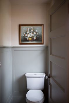 a white toilet sitting in a bathroom next to a framed flower arrangement on the wall