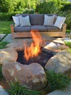 an outdoor fire pit surrounded by rocks and grass with pillows on it's sides