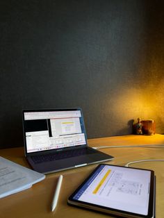 an open laptop computer sitting on top of a wooden desk next to a tablet pc