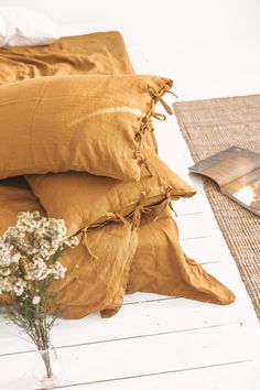 a vase with some flowers sitting on top of it next to pillows and a book