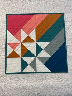 a quilted wall hanging on the side of a bed with an orange and blue design