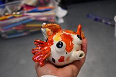 a hand holding a ceramic fish figurine in the shape of a goldfish