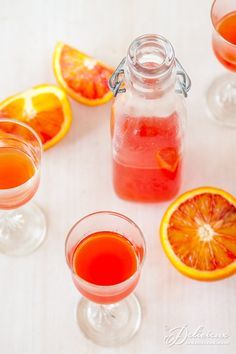 three glasses filled with liquid next to sliced oranges and another glass full of juice