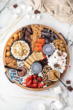 a wooden platter filled with assorted snacks and marshmallows on a marble table