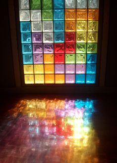 the light is shining on the floor in front of a window with colored glass blocks