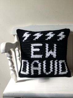 a black and white crocheted pillow sitting on top of a white chair next to a wall