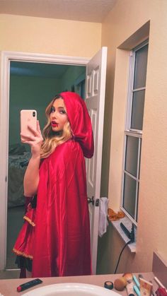 a woman in a red robe is taking a selfie with her cell phone while standing in front of the mirror