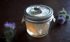 a glass jar filled with liquid sitting on top of a table next to some flowers