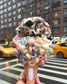 someone holding up an ice cream cone filled with cereal and marshmallows on a city street