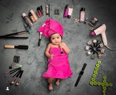 a baby in a pink dress surrounded by cosmetics