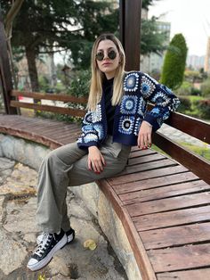 a woman is sitting on a wooden bench wearing sunglasses and a sweater with an ornament pattern