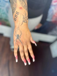 a woman's hand with a spider tattoo on her left arm and red fingernails