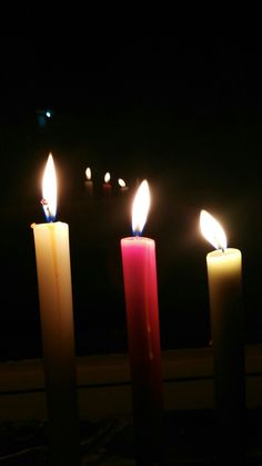 three lit candles sitting next to each other in front of a window at night time