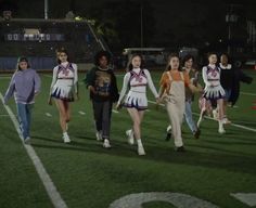 several cheerleaders are walking on the field at night with their hands in each other's pockets