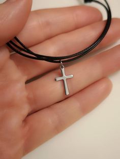 a person wearing a black leather bracelet with a cross pendant on it's wrist