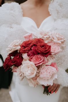 a bride holding a bouquet of red and pink flowers on her wedding day at the park